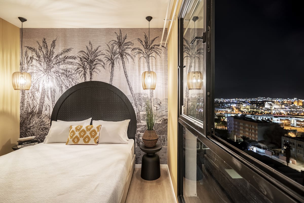 Une chambre moderne avec un grand lit, une vue sur la ville et un mur décoratif.