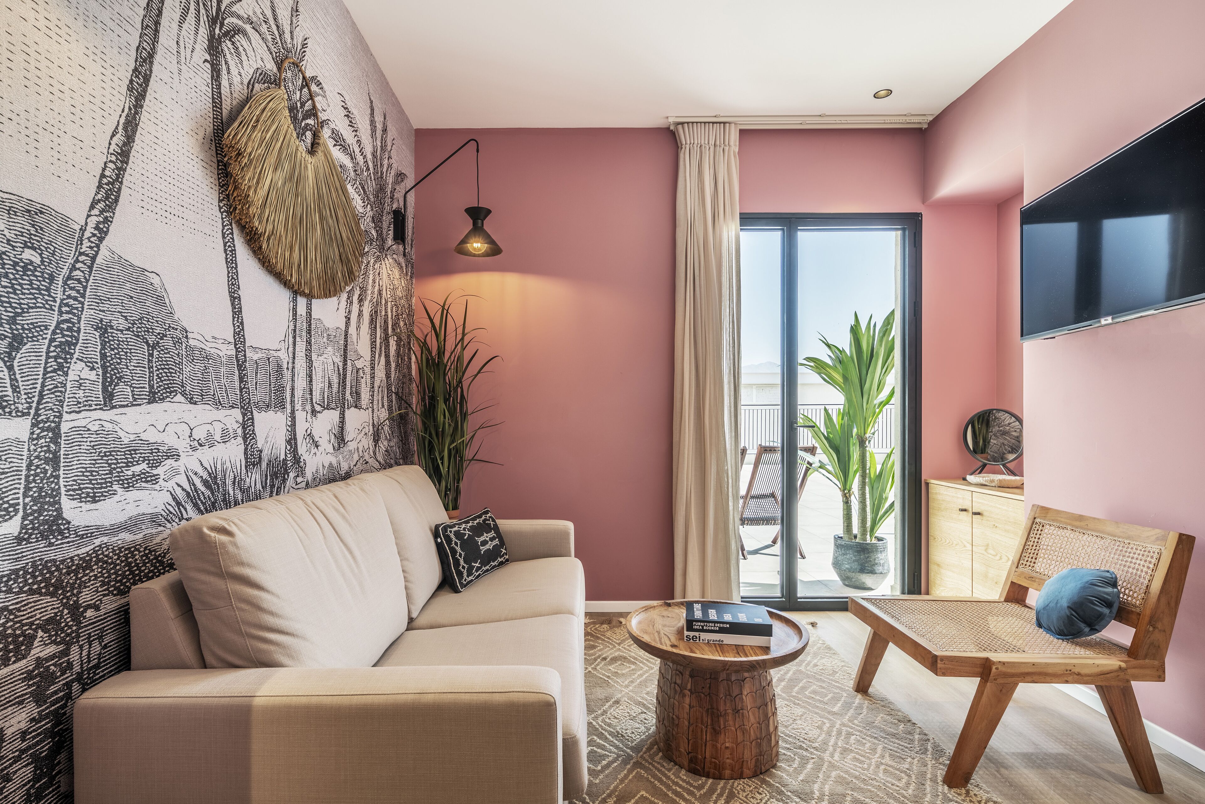 Un salon comprenant un canapé, une chaise en bois, une table basse, un téléviseur fixé au mur et une grande fenêtre avec des rideaux.