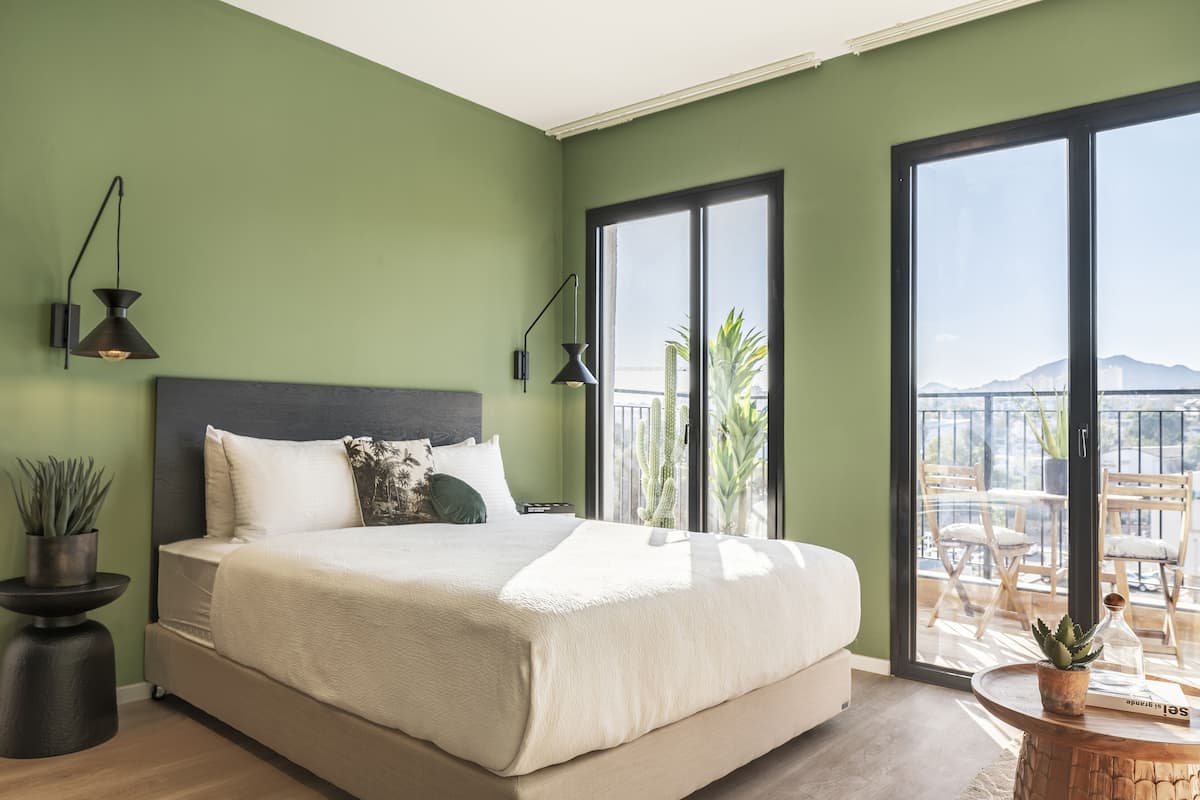 Une chambre avec un grand lit, une table de chevet, une plante en pot et une vue sur le balcon.