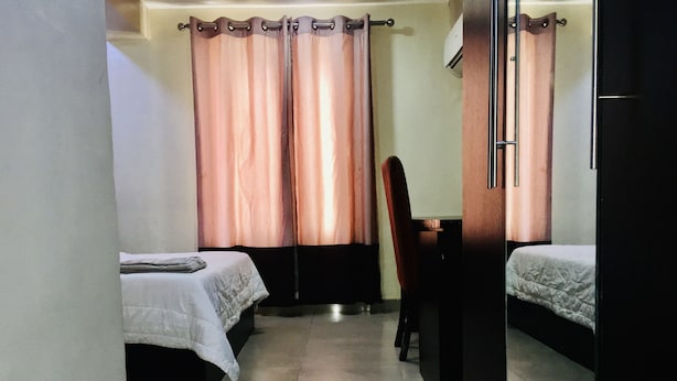 A small, dimly lit room with two beds, a chair, and a desk. - Demiral Hotel Ikeja (Lagos)