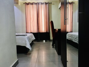 A small, dimly lit room with two beds, a chair, and a desk. - Demiral Hotel Ikeja (Lagos)