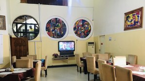 A dining area with round tables and chairs, a television on the wall, and artwork on the walls. - Demiral Hotel Ikeja (Lagos)
