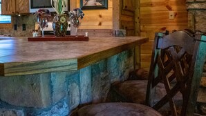 Um interior rústico em madeira, com balcão de pedra, cadeiras de madeira e iluminação pendente.