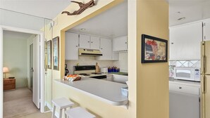 A modern kitchen with white cabinets, a central island with stools, a microwave, and a refrigerator. - Sweeping ocean and bayviews, large outdoor pool,2 Br/2 Ba. (Ocean City)