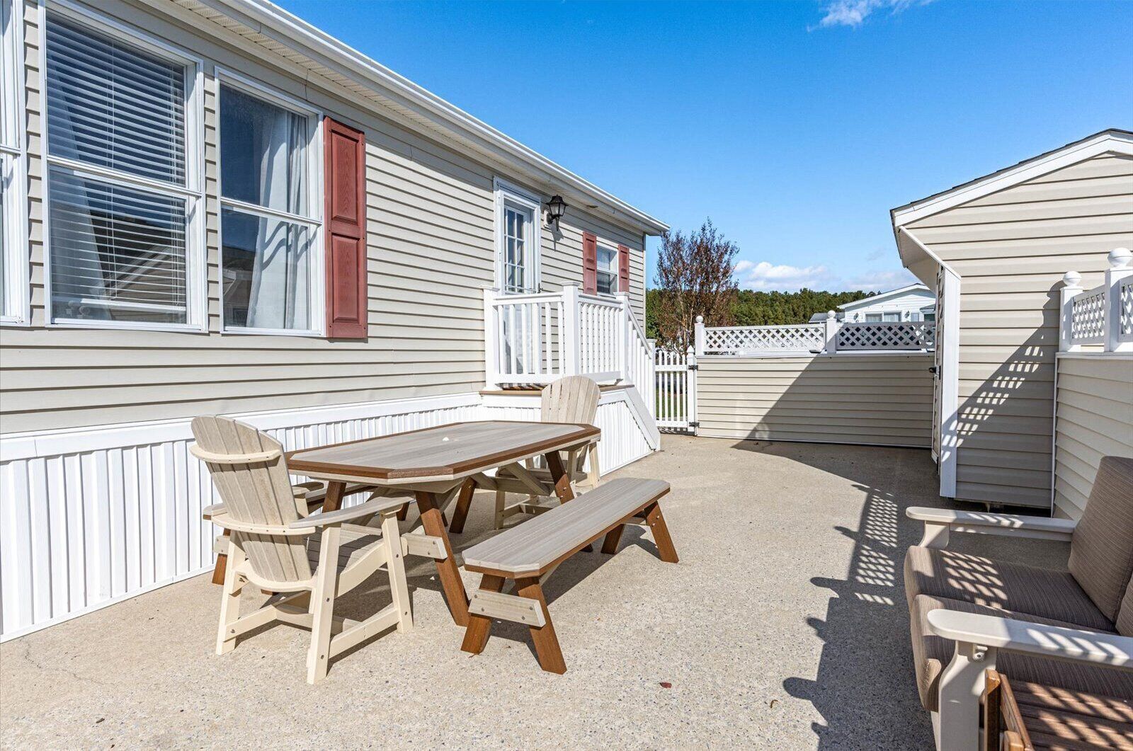 Une maison mobile dotée d’un espace patio comprenant une table et des chaises en bois, un banc et une petite terrasse.