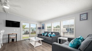 Un salon moderne avec un canapé gris, une table basse blanche et un téléviseur fixé au mur.