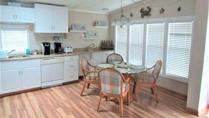A kitchen with white cabinets, a dining table with chairs, and a window with blinds.