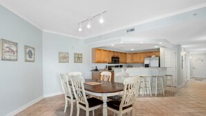 A dining area with a round table and chairs, a kitchen in the background, and artwork on the walls. - Beautiful, with a great floor plan, in down town OC, walk to beach &boards, has an outdoor pool. (Ocean City)