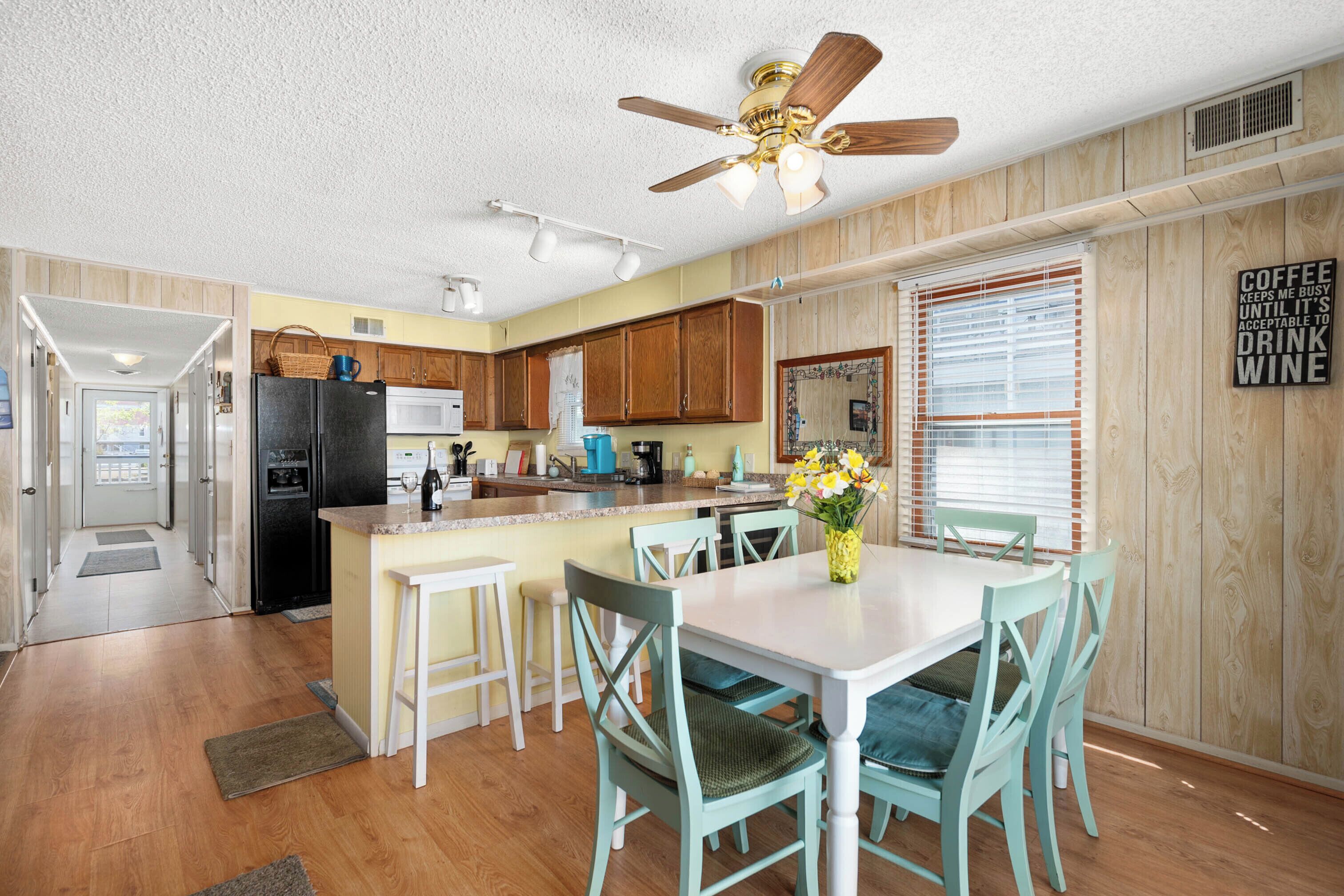 A kitchen with wooden cabinets, a refrigerator, a stove, and a ceiling fan. There is a dining table with chairs and a vase of flowers.