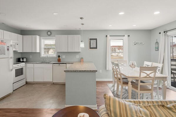 A modern kitchen with white cabinets, a central island, and a dining area with a table and chairs. - Lovely, Remodeled 2 br /2 bath @ 37th St bayside. First floor unit, has outdoor pool. (Ocean City)