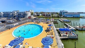 A pool area with lounge chairs and umbrellas, a dock with boats, and a view of the cityscape in the background.