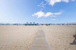 A sandy beach with a wooden walkway leading to a building with multiple umbrellas. - Split level floor plan, on the beach and boards at 4th St. Great oceanviews, has outdoor pool. (Ocean City)