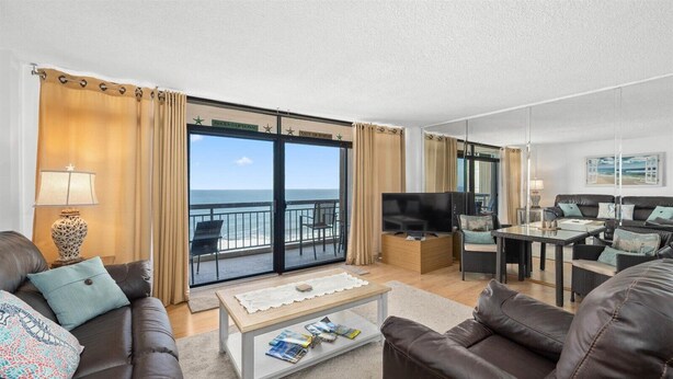 A spacious living room with a large window offering a view of the sea, a flat-screen TV, and a comfortable seating area with leather sofas and a coffee table.
