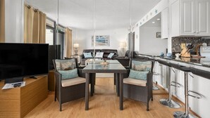 A modern kitchen with a dining area, featuring a TV, wicker chairs, and a bar area with stools.