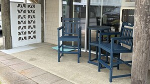 A patio area with a table and chairs, a sliding glass door, and a white fence with cut-out patterns.