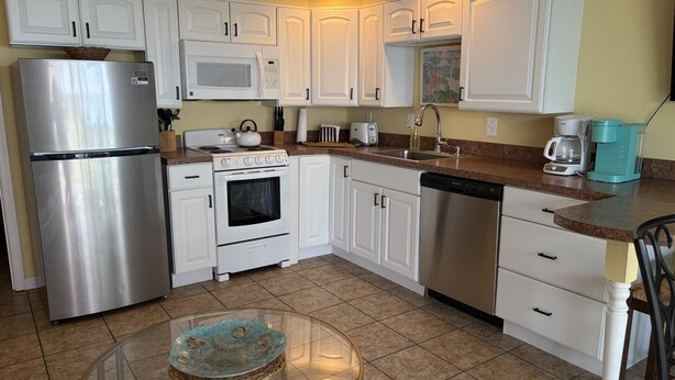 A kitchen with white cabinets, stainless steel appliances, a glass table, and a coffee maker.