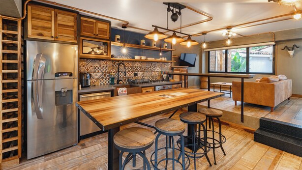 A modern kitchen with a stainless steel refrigerator, wooden bar stools, and a large wooden table. - Designer Provenza Flat (Medellín)