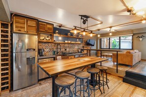 Une cuisine moderne avec un réfrigérateur en acier inoxydable, des tabourets de bar en bois et une grande table en bois.