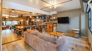 A modern kitchen with a bar area, wooden furniture, and a large TV mounted on the wall. - Designer Provenza Flat (Medellín)