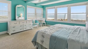 A bedroom with a bed, dresser, chair, and large windows with a view of the beach. - Ocean Colony 28 at 47th St.  4 br/ 3 ba, oceanfront townhouse with outdoor pool. (Ocean City)