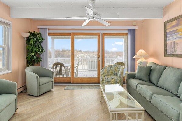 A living room with a ceiling fan, a glass coffee table, a sofa, a chair, and a large potted plant. - Ocean Colony 28 at 47th St. 4 br/ 3 ba, oceanfront townhouse with outdoor pool. (Ocean City)