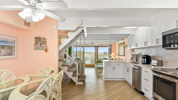 A modern kitchen with white cabinets, a stainless steel oven, and a dining area with wicker chairs and a glass table. - Ocean Colony 28 at 47th St.  4 br/ 3 ba, oceanfront townhouse with outdoor pool. (Ocean City)