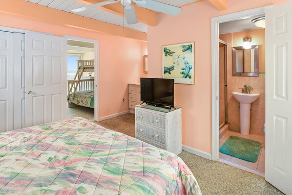 Une chambre à coucher comprenant un lit, une commode, un téléviseur, un tableau, et une salle de bain avec un lavabo et un miroir.