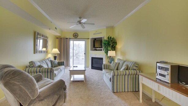 A living room with two striped couches, a small table, a ceiling fan, a fireplace, and a television. - Beautiful condo, located 61st St ocean block. 3 br, with outdoor pool. (Ocean City)