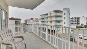 A balcony with a white chair, a white railing, and a view of multi-story buildings in the background. - Beautiful condo, located 61st St ocean block. 3 br, with outdoor pool. (Ocean City)