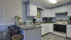 A kitchen with white cabinets, a granite countertop, a stove, and a coffee maker.