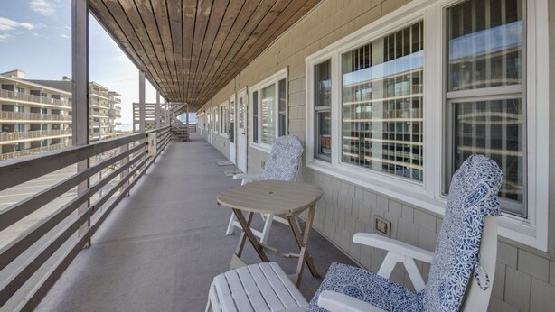A covered balcony with wooden railings, white-framed windows, and patterned outdoor chairs.