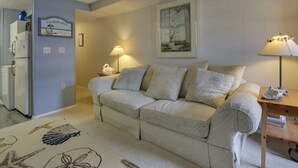 A living room with a beige sofa, a small table, a lamp, and a framed picture on the wall.