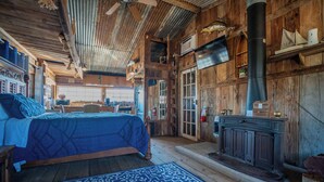 A rustic wooden room with a bed, a fireplace, and a large window.
