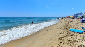 A beach with clear skies, people swimming and walking along the shore, and beach umbrellas and lounge chairs.