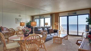 A spacious living area with a large window overlooking the sea, furnished with a sofa, chairs, and a dining table.