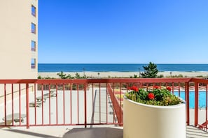 Un balcon avec vue sur la plage et l’océan, une piscine et un jardinier avec des fleurs.