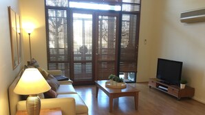 A living room with a sofa, a coffee table with plants, a TV on a stand, and a lamp on a side table. - Central Loft Apartment Free Parking (Canberra)