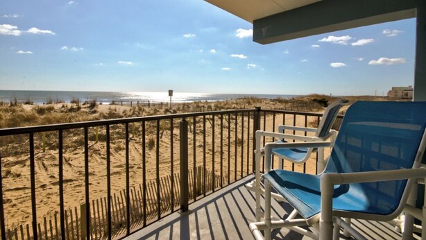A balcony with blue chairs overlooking a beach with sand dunes and a fence. - Sand Trap 102 - 2br/2ba oceanfront in area of low beach congestion. (Ocean City)