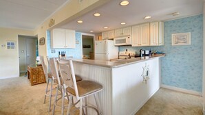 A kitchen with white cabinets, a central island with bar stools, a microwave, and a refrigerator. - Sand Trap 102 - 2br/2ba oceanfront in area of low beach congestion. (Ocean City)