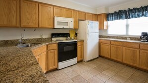 Una cocina con armarios de madera, microondas, refrigerador, estufa y ventana con cortina.