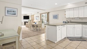 A modern kitchen with white cabinets, a dining area with a table and chairs, and a TV in the background.