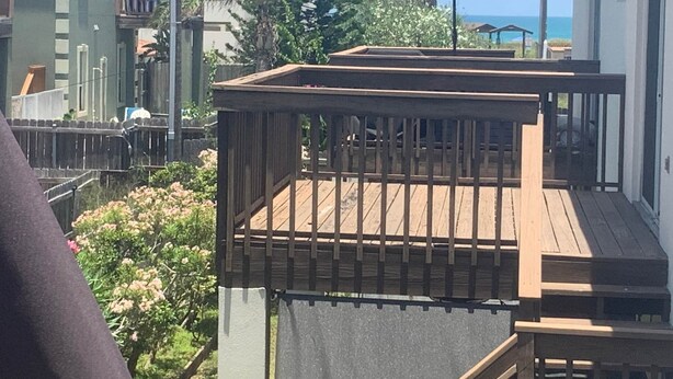 Une terrasse en bois avec une rambarde, un parasol bleu et une vue sur l’océan.