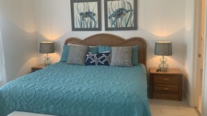 Une chambre à coucher avec une couvre-lit turquoise, une tête de lit en osier, deux lampes fixées au mur et deux tableaux représentant des hippocampes, encadrés.