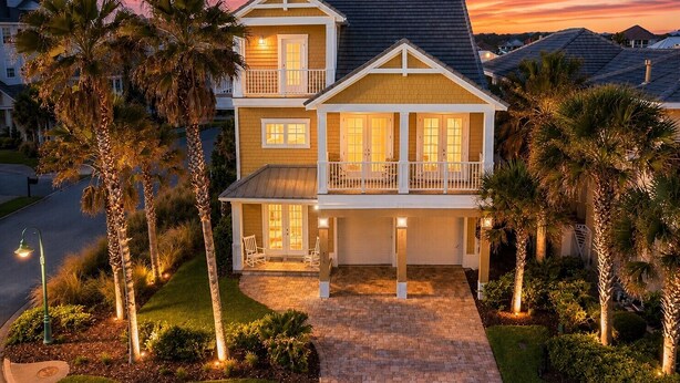 Een tweelaags huis met balkon, omgeven door palmbomen en een pad van baksteen.