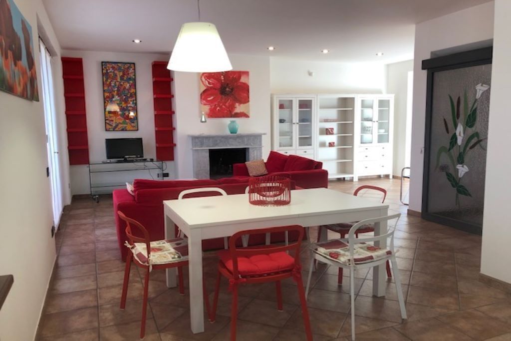 A dining area with a white table and red chairs, a red sofa, and a fireplace.