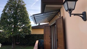 Et hus med en overdækket terrasse, en hængende gyngestol og en lampe monteret på væggen.
