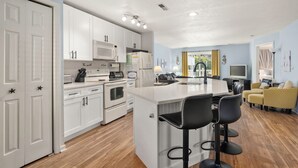 A modern kitchen with white cabinets, a central island with bar stools, and a dining area with yellow chairs.