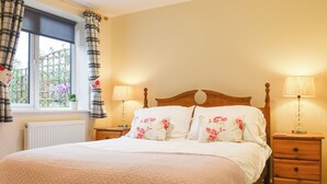 A neatly made bed with floral bedding, two bedside lamps, a wooden nightstand, and a window with curtains.