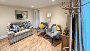 A living room with a sofa, two armchairs, a floor lamp, a TV stand with a remote, and a decorative metal piece.