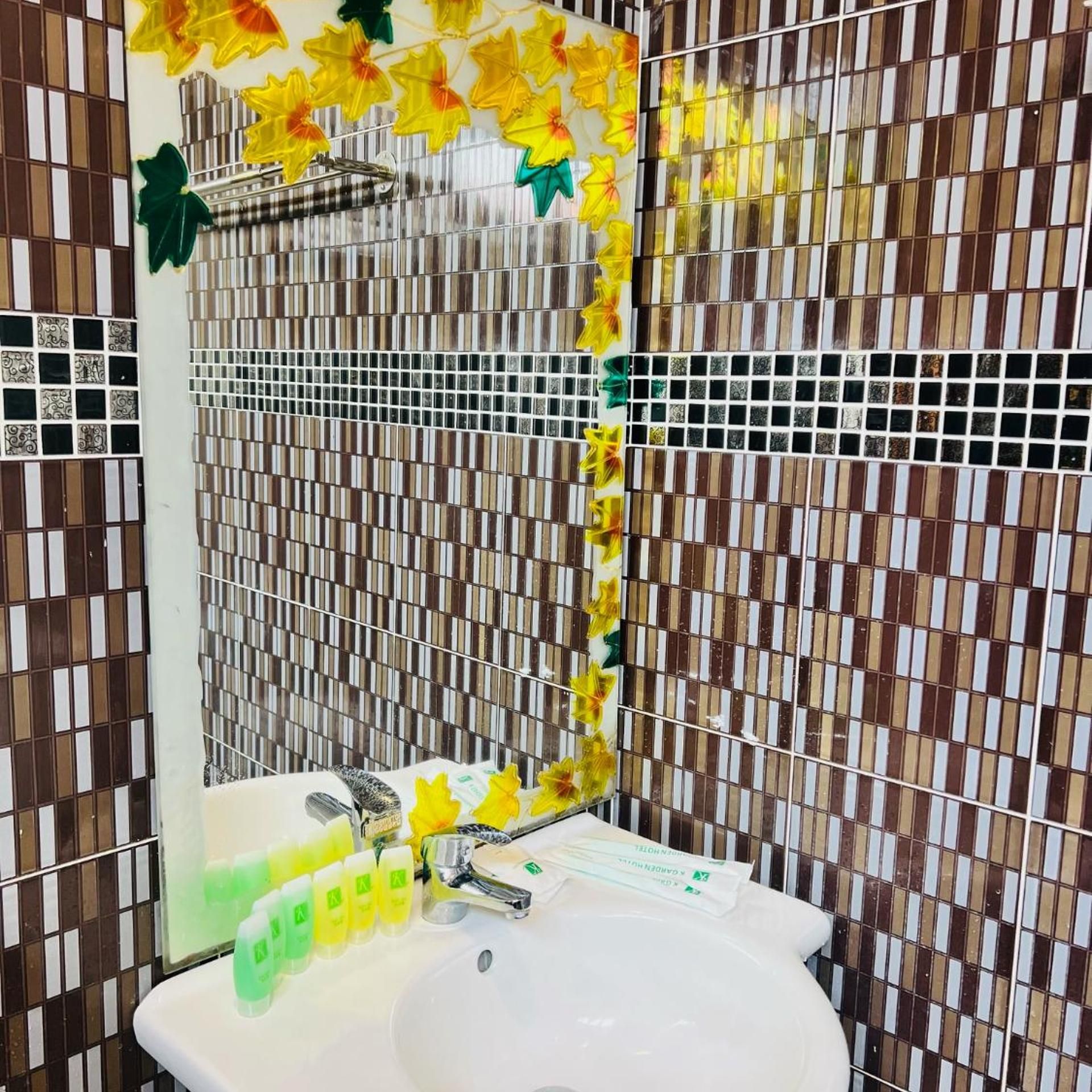 A bathroom with a white sink, a mirror, and a tiled wall with a pattern of brown and beige tiles.